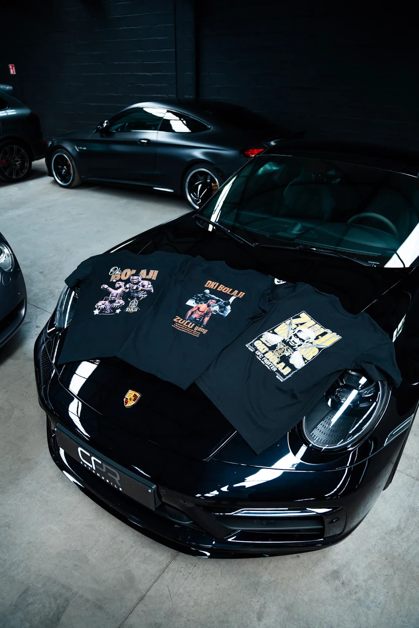 Trois tees Zulu Gang posés sur le capot d’une Porsche noire